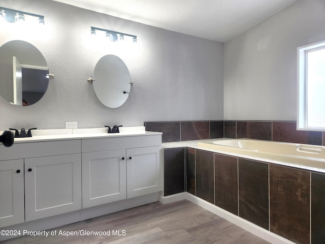 bathroom featuring hardwood / wood-style floors, vanity, and tiled tub