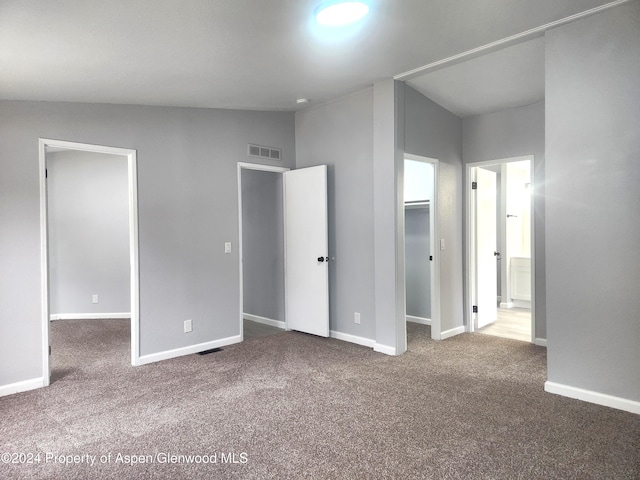 unfurnished bedroom featuring a walk in closet, carpet floors, vaulted ceiling, and a closet