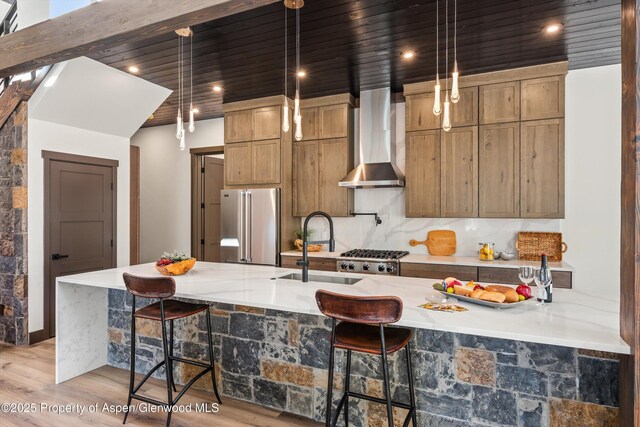 129 Sage Meadow Rd, Glenwood Springs, CO 81601 - kitchen with appliances with stainless steel finishes, a sink, light wood-style floors, a breakfast bar, and wall chimney exhaust hood