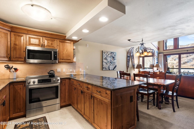 kitchen featuring kitchen peninsula, appliances with stainless steel finishes, an inviting chandelier, dark stone countertops, and light tile patterned flooring