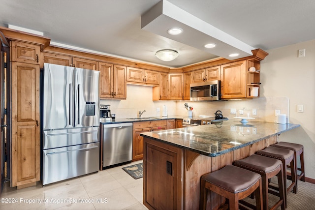 kitchen featuring dark stone counters, sink, light tile patterned flooring, kitchen peninsula, and stainless steel appliances