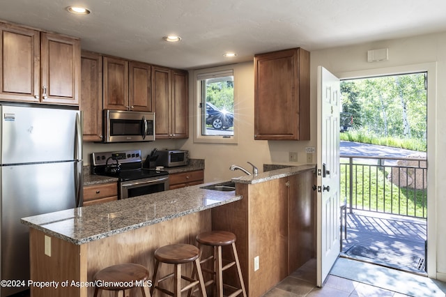 kitchen featuring sink, stainless steel appliances, light stone counters, plenty of natural light, and a breakfast bar area