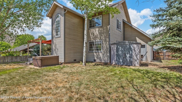 back of house with a storage unit, a yard, and a hot tub