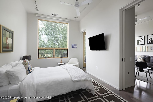 bedroom with ceiling fan, rail lighting, dark wood finished floors, baseboards, and visible vents