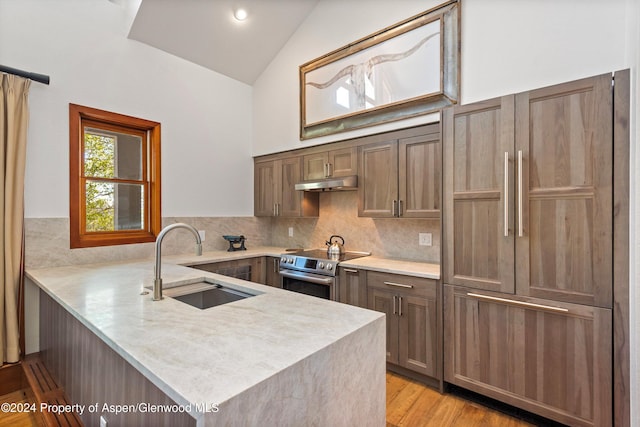 kitchen with kitchen peninsula, sink, paneled built in refrigerator, stainless steel electric range oven, and lofted ceiling