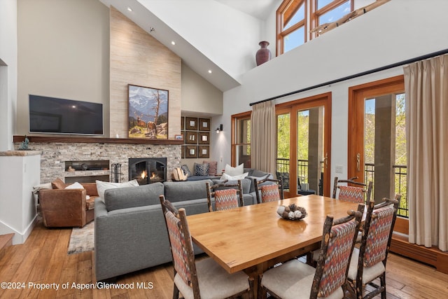 dining space featuring light hardwood / wood-style floors, a fireplace, high vaulted ceiling, and french doors