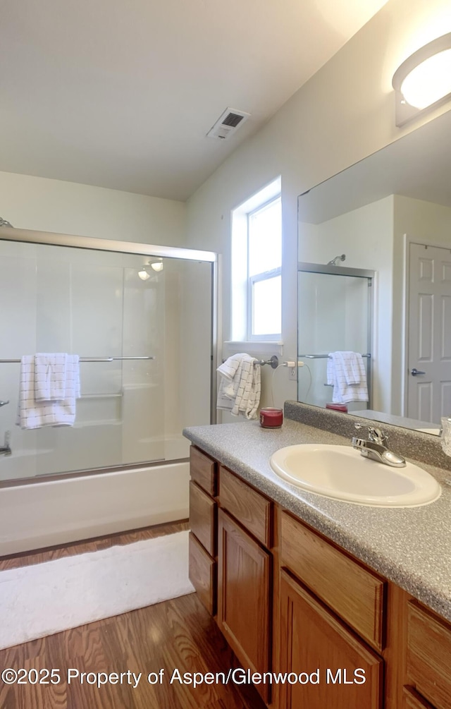 bathroom with vanity, hardwood / wood-style floors, and bath / shower combo with glass door