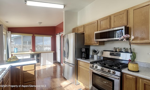 kitchen with vaulted ceiling, appliances with stainless steel finishes, wine cooler, and light hardwood / wood-style flooring