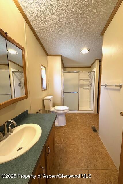 full bathroom featuring toilet, a stall shower, ornamental molding, a textured ceiling, and vanity