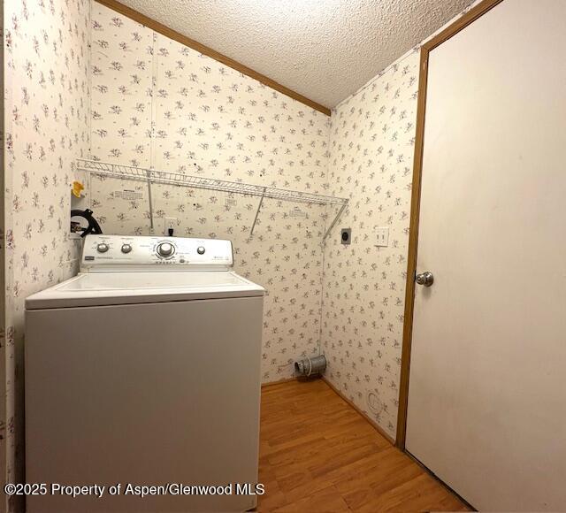 laundry area featuring wood finished floors, wallpapered walls, laundry area, washer / clothes dryer, and a textured ceiling