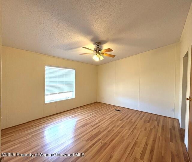 spare room with a textured ceiling, ceiling fan, and light wood finished floors