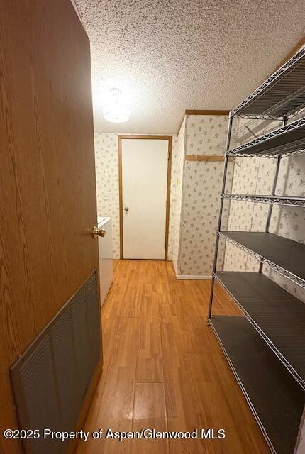 corridor with visible vents, wallpapered walls, a textured ceiling, and light wood-style floors