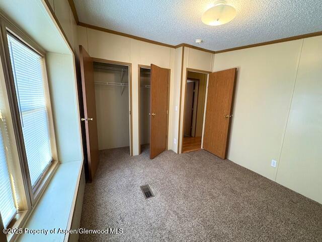 unfurnished bedroom with crown molding, carpet, visible vents, and a textured ceiling