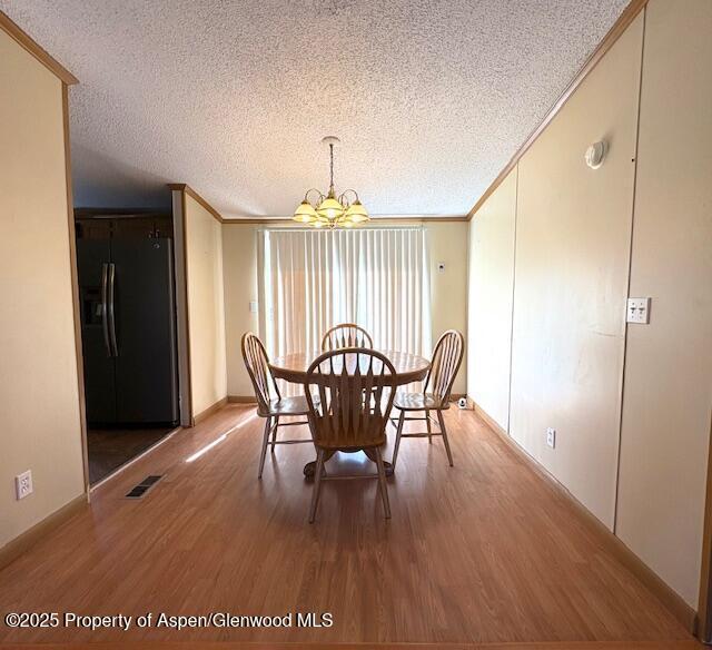 dining area featuring visible vents, wood finished floors, a textured ceiling, and ornamental molding