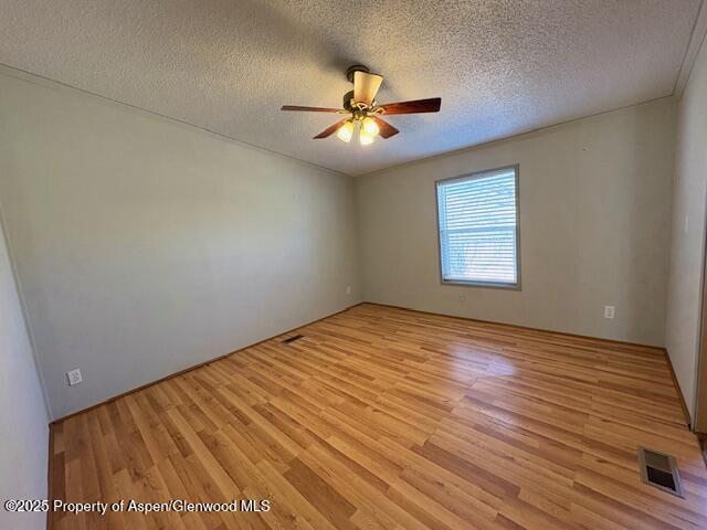 empty room with visible vents, ceiling fan, a textured ceiling, and light wood-style floors