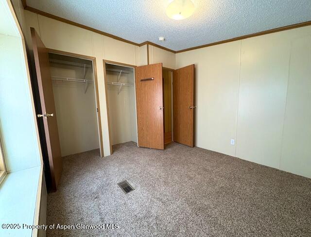 unfurnished bedroom with visible vents, two closets, ornamental molding, light carpet, and a textured ceiling