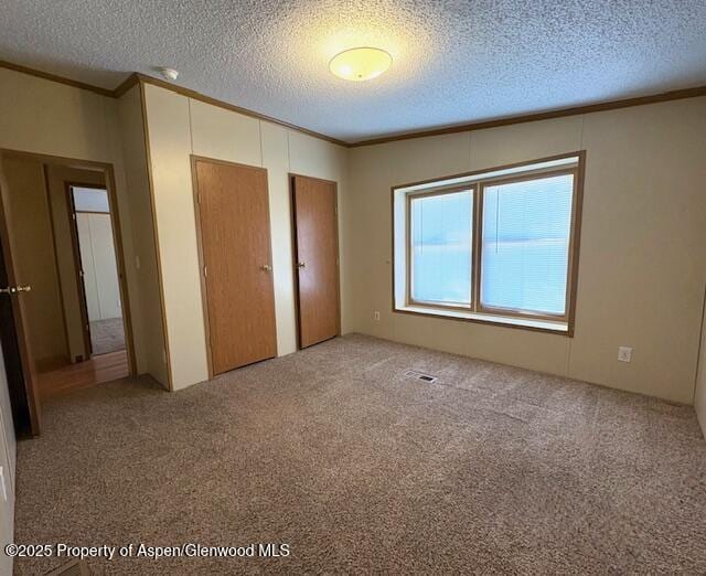 unfurnished bedroom with carpet flooring, two closets, crown molding, and a textured ceiling