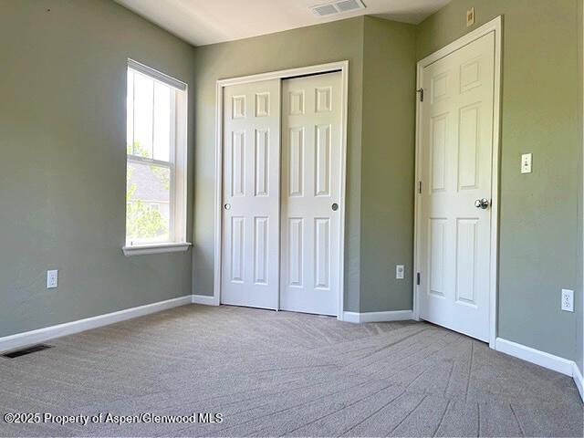 unfurnished bedroom with carpet floors, visible vents, baseboards, and a closet