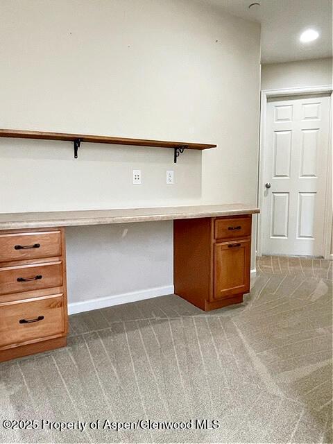 unfurnished office featuring dark colored carpet, built in study area, and baseboards