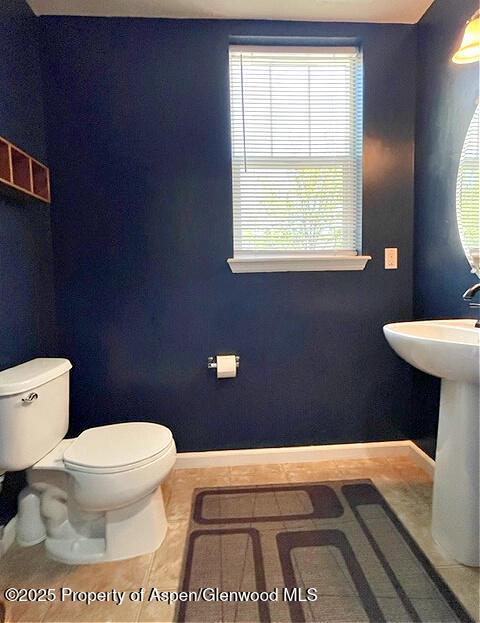 half bath featuring tile patterned flooring, toilet, and baseboards