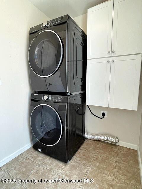 washroom with light tile patterned flooring, stacked washing maching and dryer, cabinet space, and baseboards