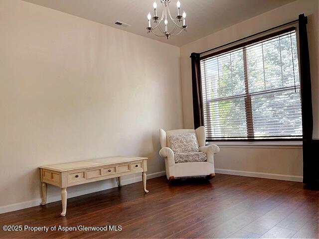 unfurnished room with visible vents, a notable chandelier, baseboards, and wood finished floors