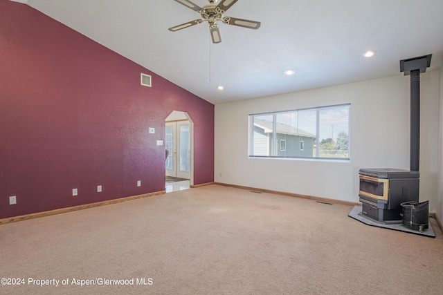 unfurnished living room with carpet flooring, ceiling fan, a wood stove, and vaulted ceiling