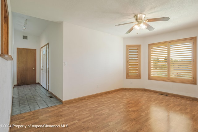 unfurnished room with ceiling fan, light wood-type flooring, and a textured ceiling