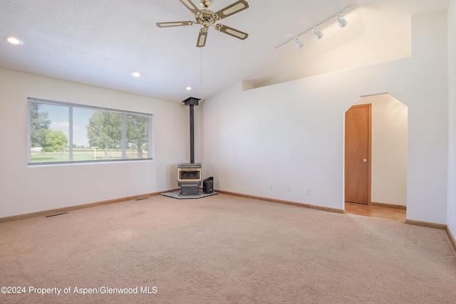 unfurnished living room featuring a wood stove, light carpet, rail lighting, and lofted ceiling