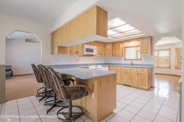 kitchen featuring light brown cabinets, stove, light colored carpet, kitchen peninsula, and a breakfast bar area