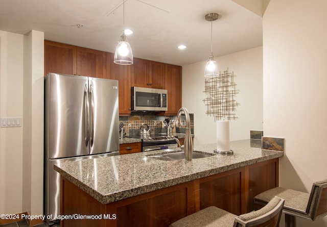 kitchen with sink, kitchen peninsula, stone countertops, decorative light fixtures, and appliances with stainless steel finishes