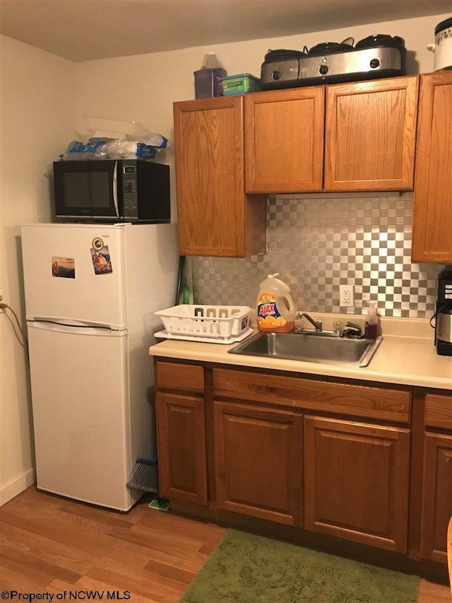 kitchen featuring tasteful backsplash, light hardwood / wood-style floors, sink, and white refrigerator