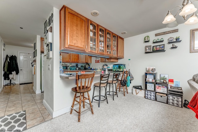 kitchen with an inviting chandelier, decorative light fixtures, a kitchen breakfast bar, kitchen peninsula, and light colored carpet