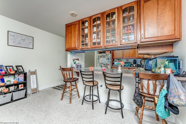 interior space with dark stone counters, stainless steel fridge, a breakfast bar area, and light colored carpet