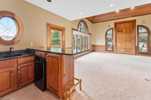 kitchen with light carpet, sink, kitchen peninsula, and dark stone counters