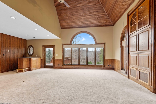 unfurnished living room with ceiling fan, a towering ceiling, wooden walls, carpet, and wooden ceiling