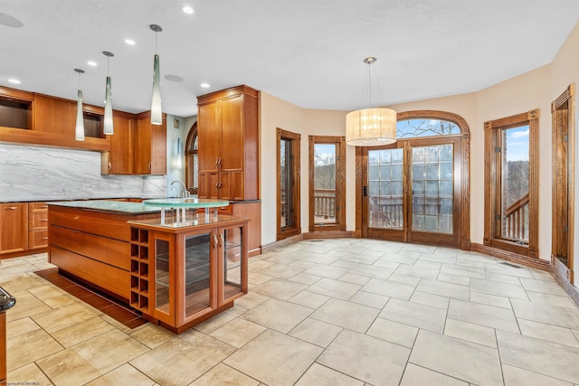 kitchen featuring light stone countertops, a center island with sink, decorative backsplash, and decorative light fixtures