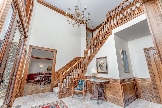 staircase featuring an inviting chandelier, ornamental molding, light tile floors, and a high ceiling