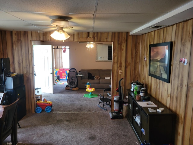 interior space featuring a paneled ceiling, wooden walls, and ceiling fan