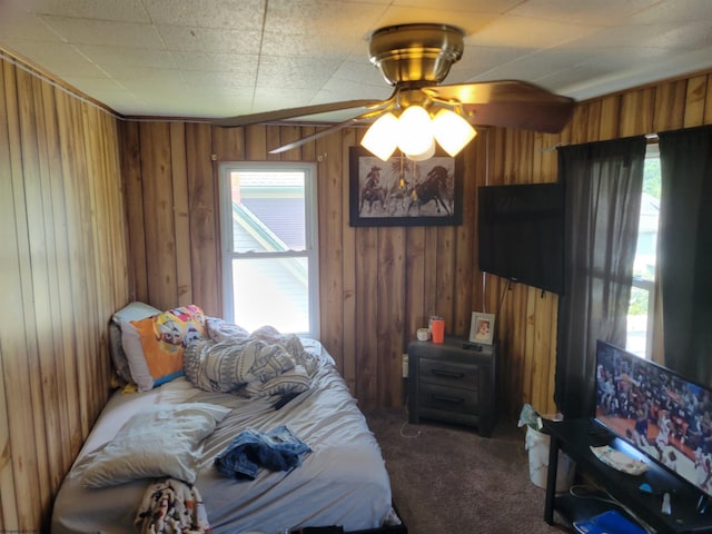 bedroom with wooden walls, multiple windows, dark colored carpet, and ceiling fan