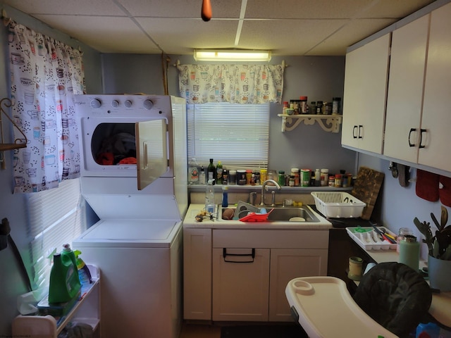 kitchen with sink, a drop ceiling, stacked washer / drying machine, and white cabinets