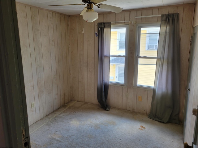 spare room with ceiling fan, light carpet, and wood walls