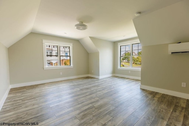 additional living space featuring lofted ceiling, an AC wall unit, and wood-type flooring