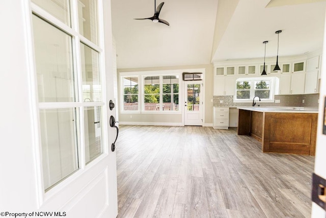 kitchen with ceiling fan, light hardwood / wood-style flooring, white cabinets, backsplash, and hanging light fixtures