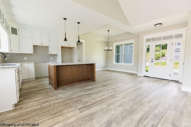 kitchen with light hardwood / wood-style floors, a notable chandelier, a kitchen island, backsplash, and sink