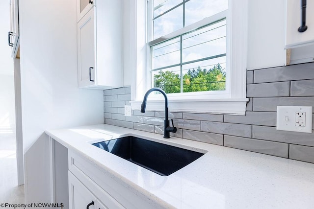 kitchen featuring white cabinets, backsplash, sink, and light stone counters