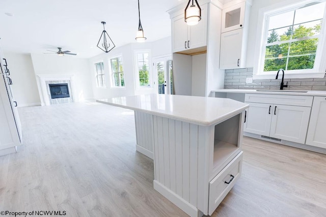 kitchen with backsplash, ceiling fan, light wood-type flooring, a high end fireplace, and a kitchen island