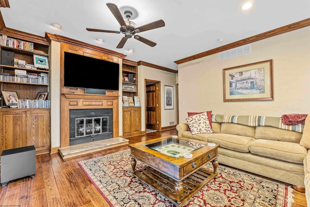 living room with built in shelves, ornamental molding, ceiling fan, and dark hardwood / wood-style flooring