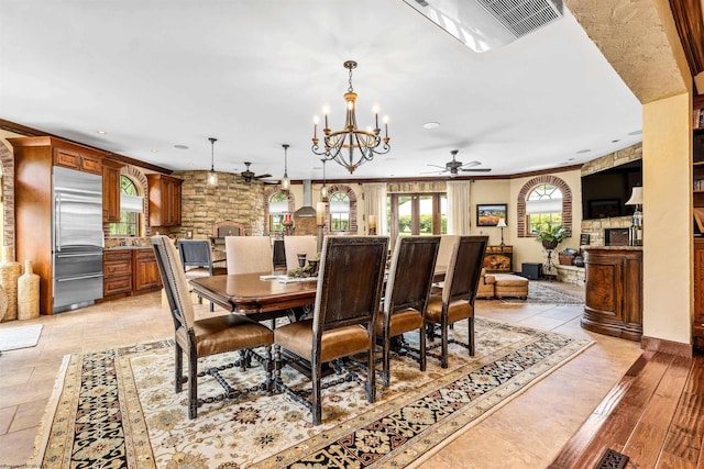 dining space featuring a fireplace, ornamental molding, light tile floors, and ceiling fan with notable chandelier