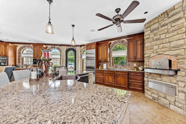 kitchen featuring hanging light fixtures, tasteful backsplash, light stone counters, ceiling fan, and a stone fireplace